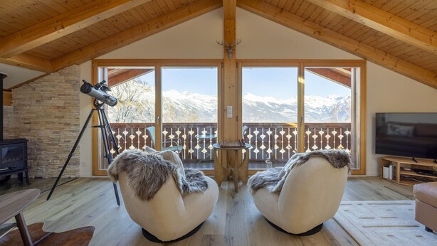 Une pièce chaleureuse avec un plafond en bois, deux fauteuils confortables recouverts de peaux, un télescope, une cheminée et un téléviseur posé sur un meuble en bois.