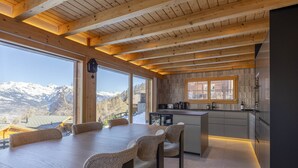 Une cuisine moderne avec des poutres en bois, de grandes fenêtres et une vue sur des montagnes enneigées.