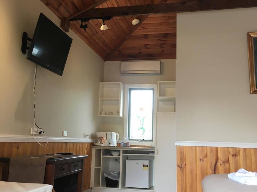 A compact room with a wooden ceiling, a flat-screen TV mounted on the wall, a kitchenette with a refrigerator, and a window with a view.