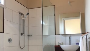 Ein modernes Badezimmer mit Duschkabine aus Glas, weißen Fliesen, Holzboden und Waschbecken in Weiß mit Spiegel darüber.