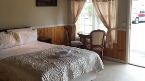 Ein Schlafzimmer mit einem großen Bett, Holzboden, einem Bild an der Wand, einem Sessel und einem Fenster mit Vorhängen.