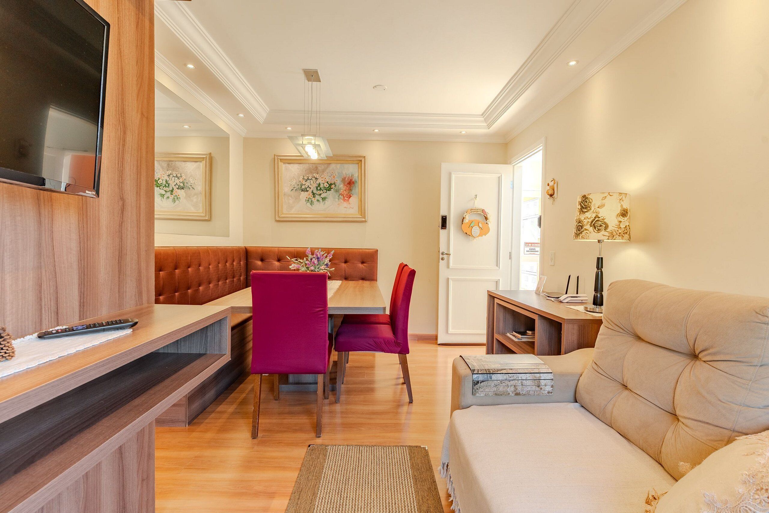A modern living room with a sofa, a dining area with a table and chairs, and a TV mounted on the wall.