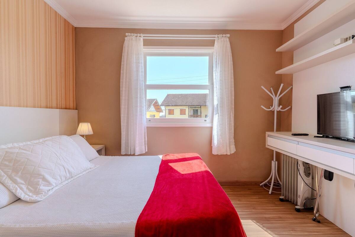 Ein Schlafzimmer mit Bett, Fernseher, Heizung und einem Fenster mit Vorhängen.