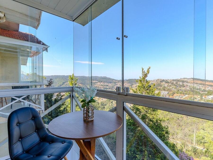 A balcony with a glass railing, a round wooden table, and a black leather chair.