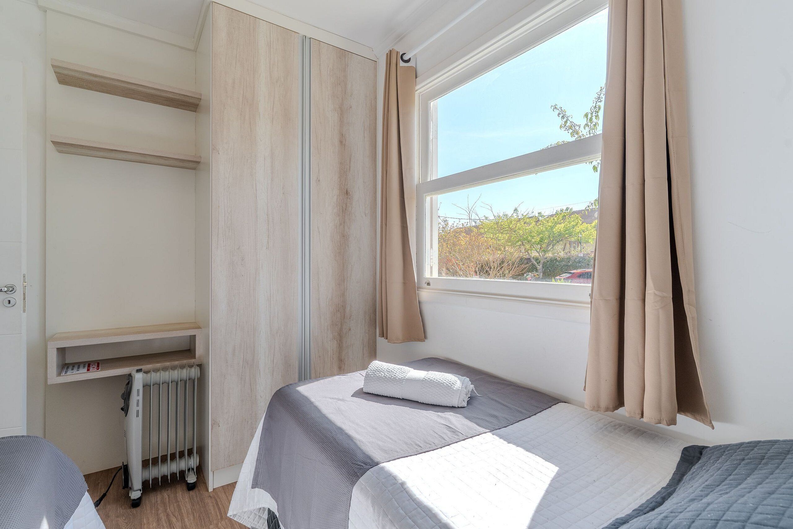 Un dormitorio con cama, un radiador, una ventana con cortinas y vistas a árboles.