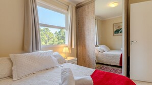 Habitación de hotel con cama, ventana con cortinas, lámpara de noche y espejo que refleja otra cama.