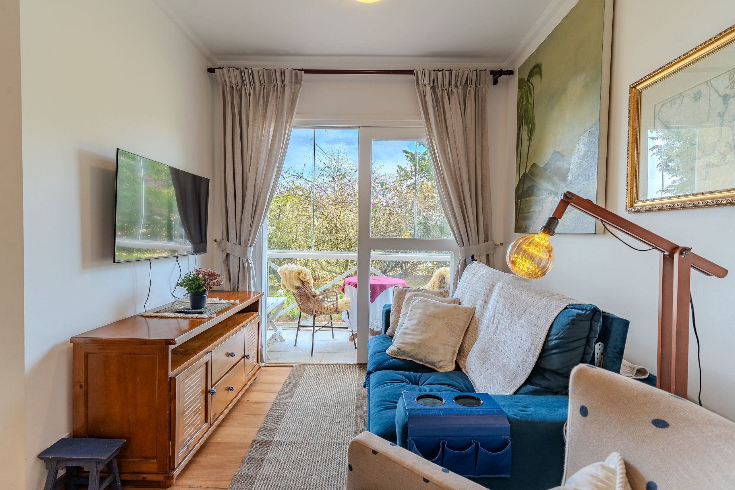 Um quarto acolhedor com um sofá azul, um armário de madeira, uma televisão e uma grande janela com cortinas.