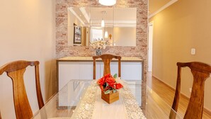 Un comedor con una mesa de vidrio, sillas de madera, un jarrón de flores y una pared de ladrillo con un espejo.