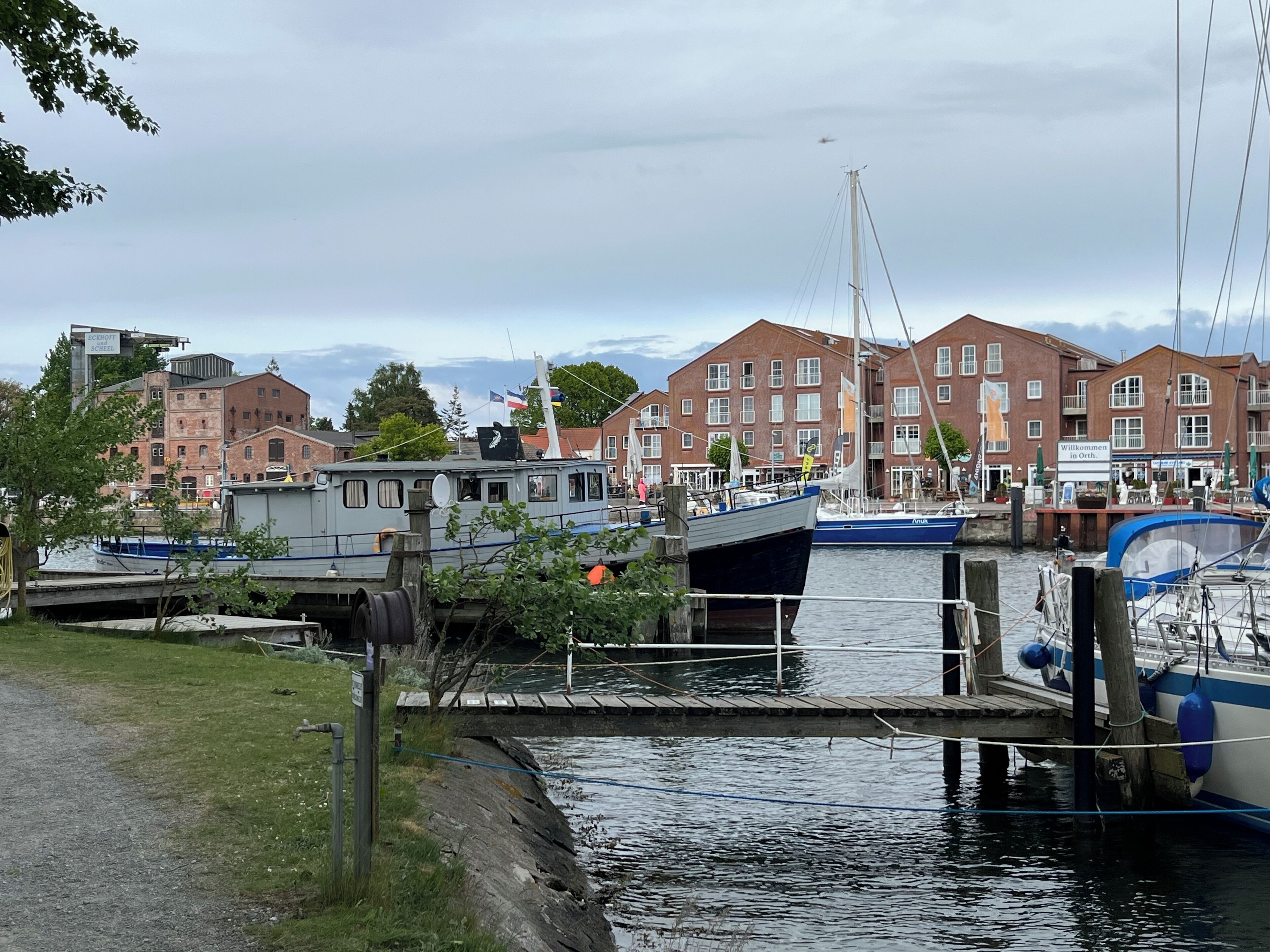 A canal with boats docked, surrounded by traditional brick buildings and a grassy area.