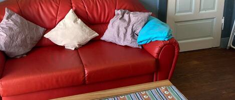 A red leather sofa with cushions, a wooden coffee table with a striped tablecloth, a remote control, and a decorative plate.