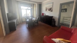 A living room with a red sofa, a dining area with a table and chairs, a TV, and a window with curtains.