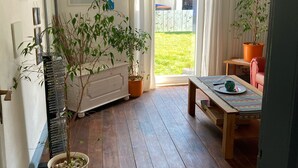 A room with a wooden floor, a table with a patterned tablecloth, a potted plant, and a radiator.
