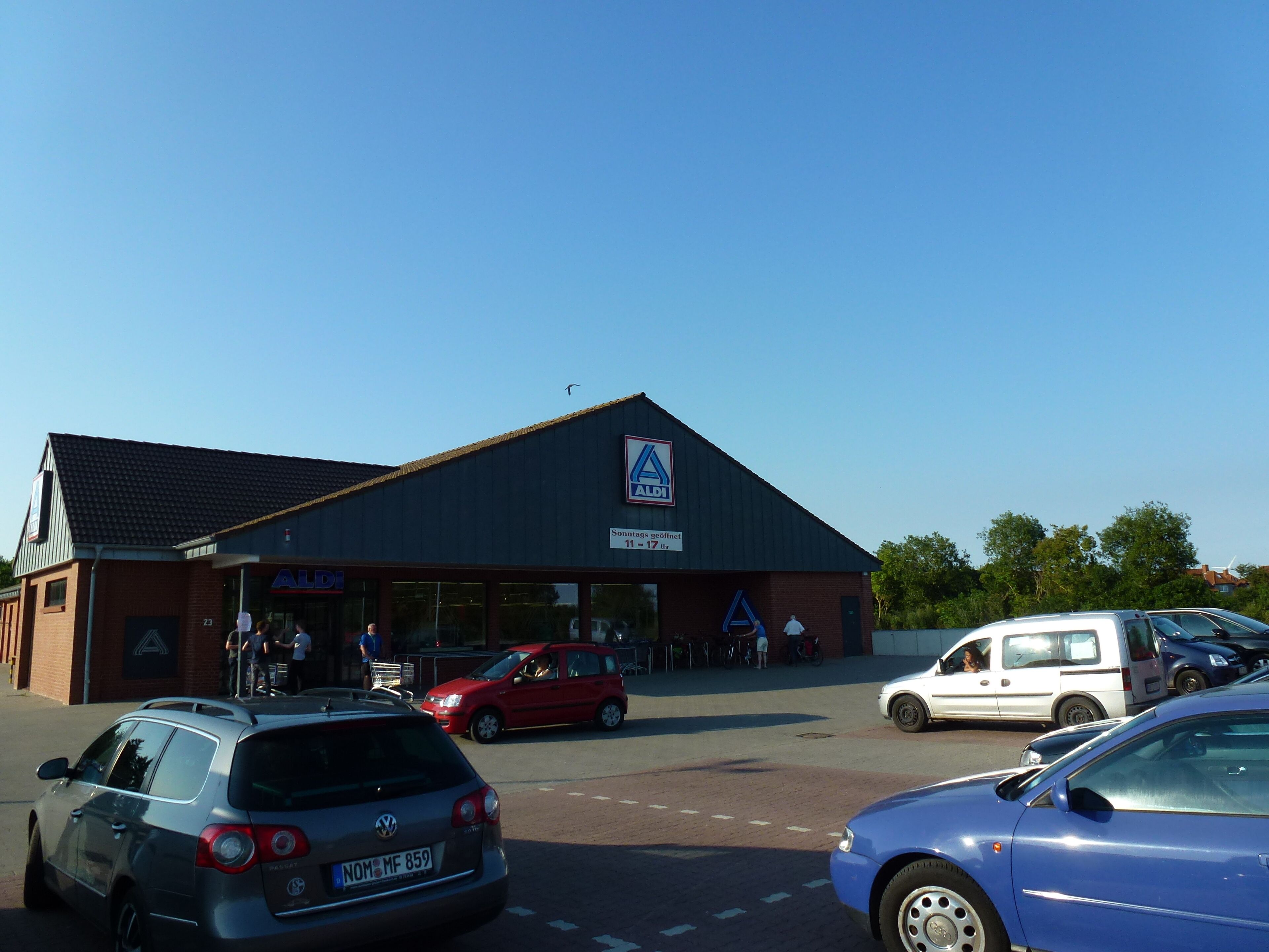 Um edifício com uma placa da ALDI e um estacionamento com vários carros.