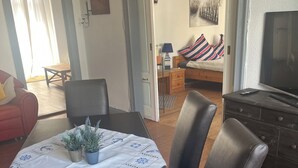 A dining area with a table set for four, a potted plant, and a view into a bedroom with a bed and a painting.