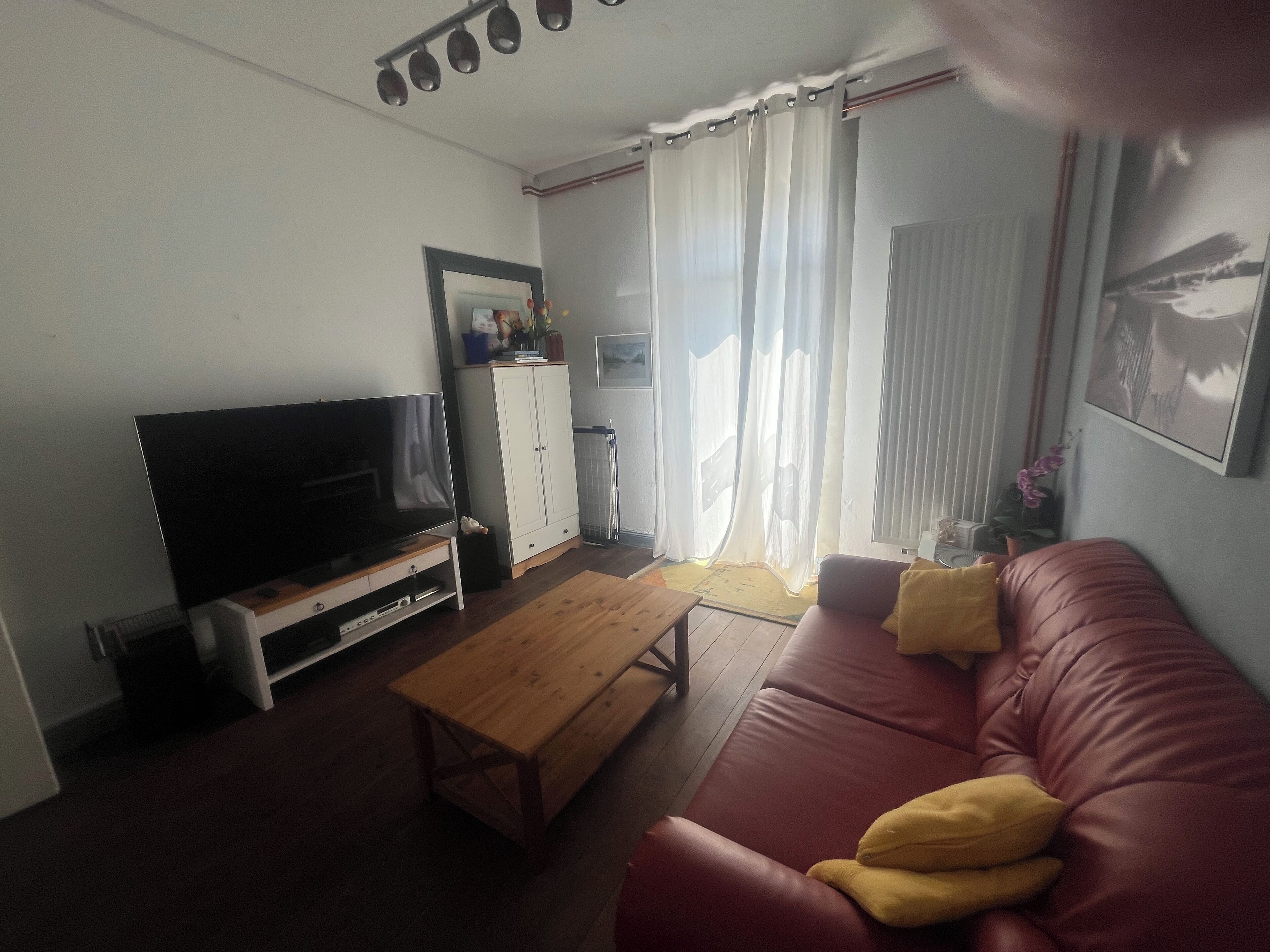 Een woonkamer met een televisie, een houten salontafel, een rode bank en een wit kastje.