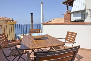 A wooden table and chairs on a balcony with a view of the sea. - Terrazza Lucilla (Cefalù)