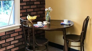 A dining area with a brick wall, a window, and a table with chairs. There is a framed picture on the wall and a vase with flowers on the table. - Cottage in Flagstaff's NoHo (Flagstaff)