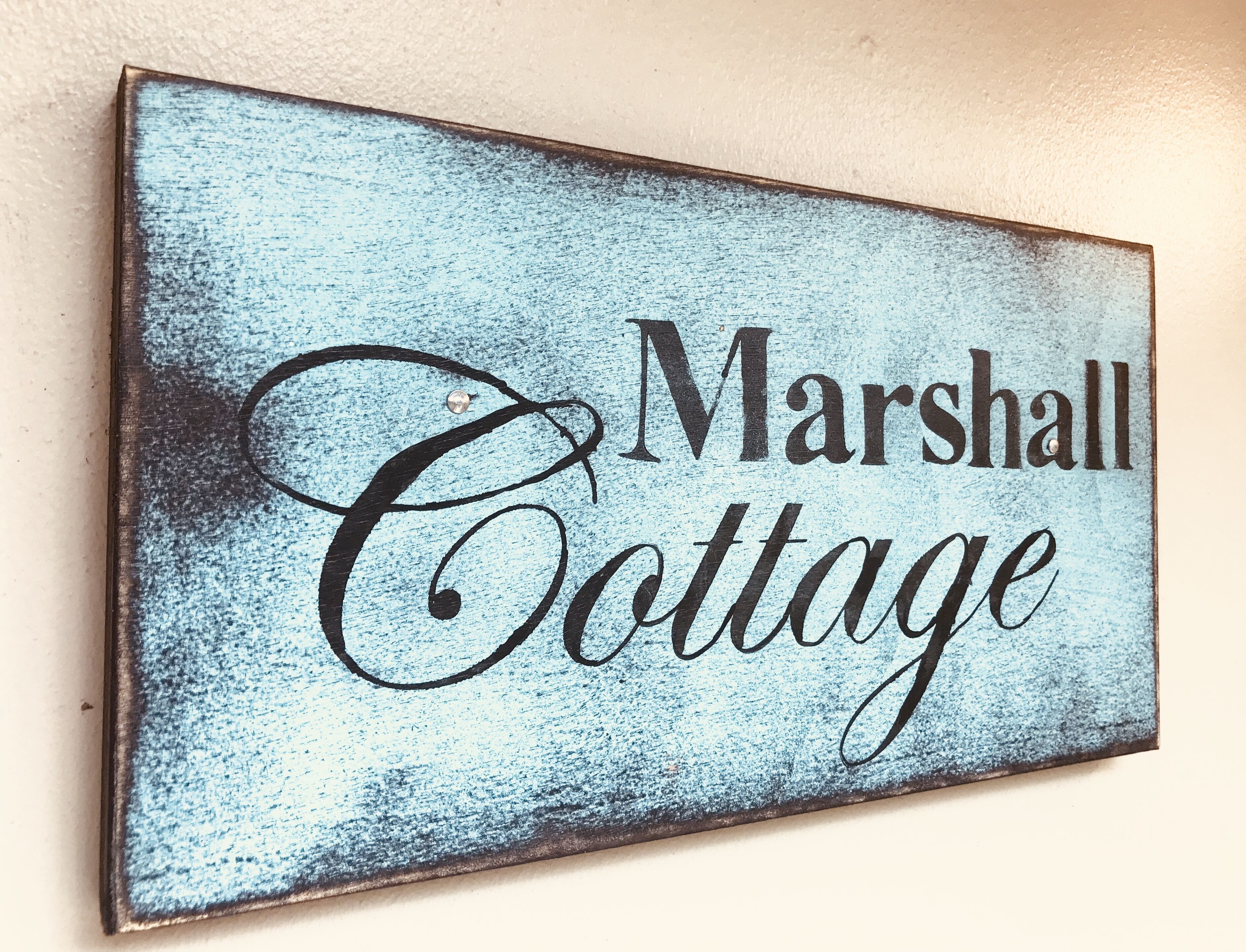 A sign with the text "Marshall Cottage" on a textured blue background.