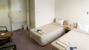 Habitación de hotel con dos camas, un escritorio, una silla, un espejo y un armario.