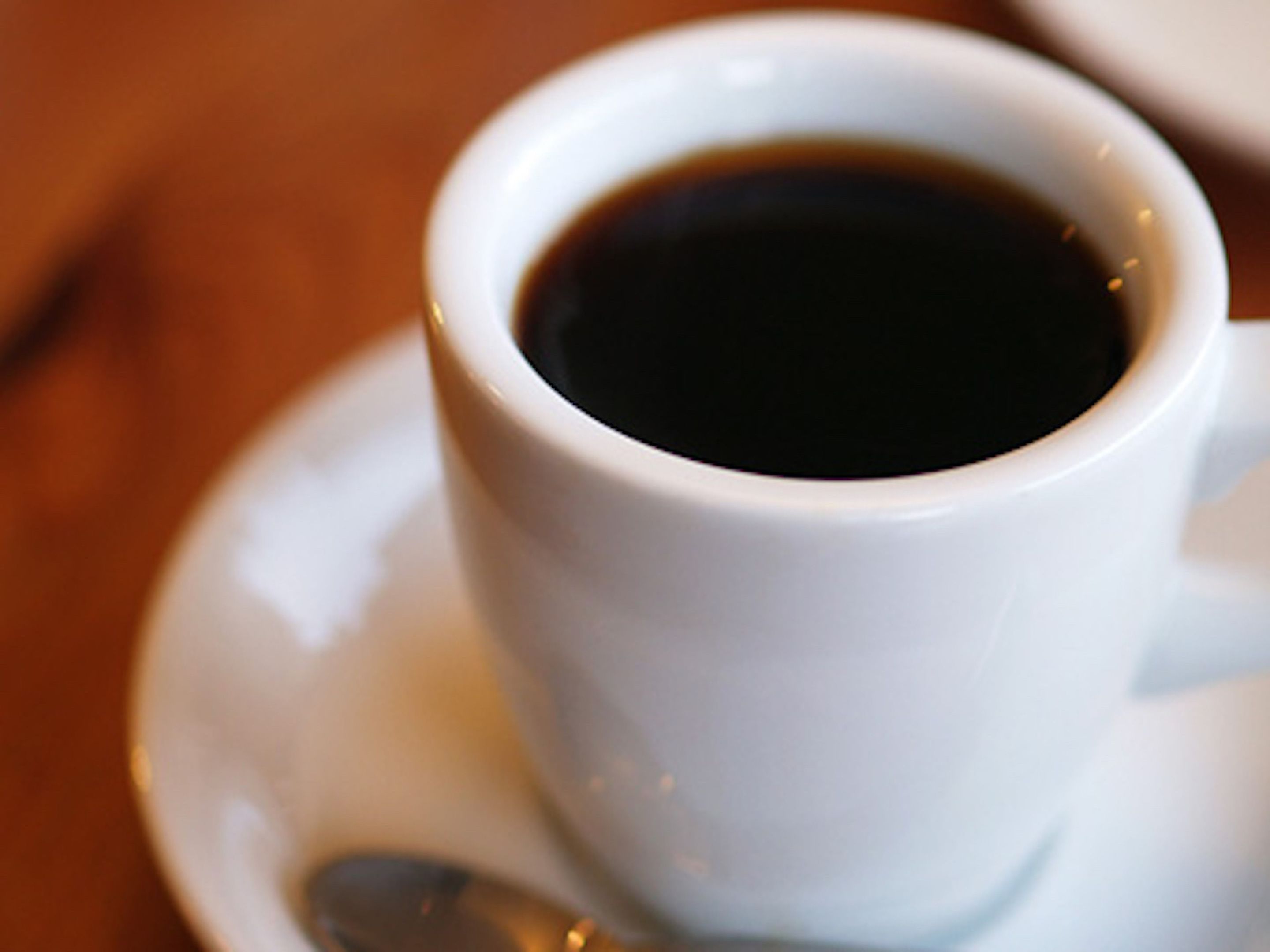 A white cup of coffee on a saucer with a spoon.