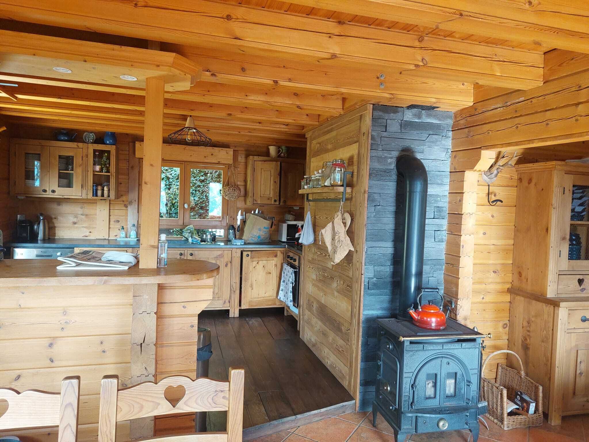 Interno rustico di una baita di legno con angolo cucina centrale, dotato di fornello, pensili in legno e una grande finestra.