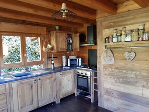A rustic kitchen with wooden cabinets, a stove, a microwave, and a hanging light fixture.