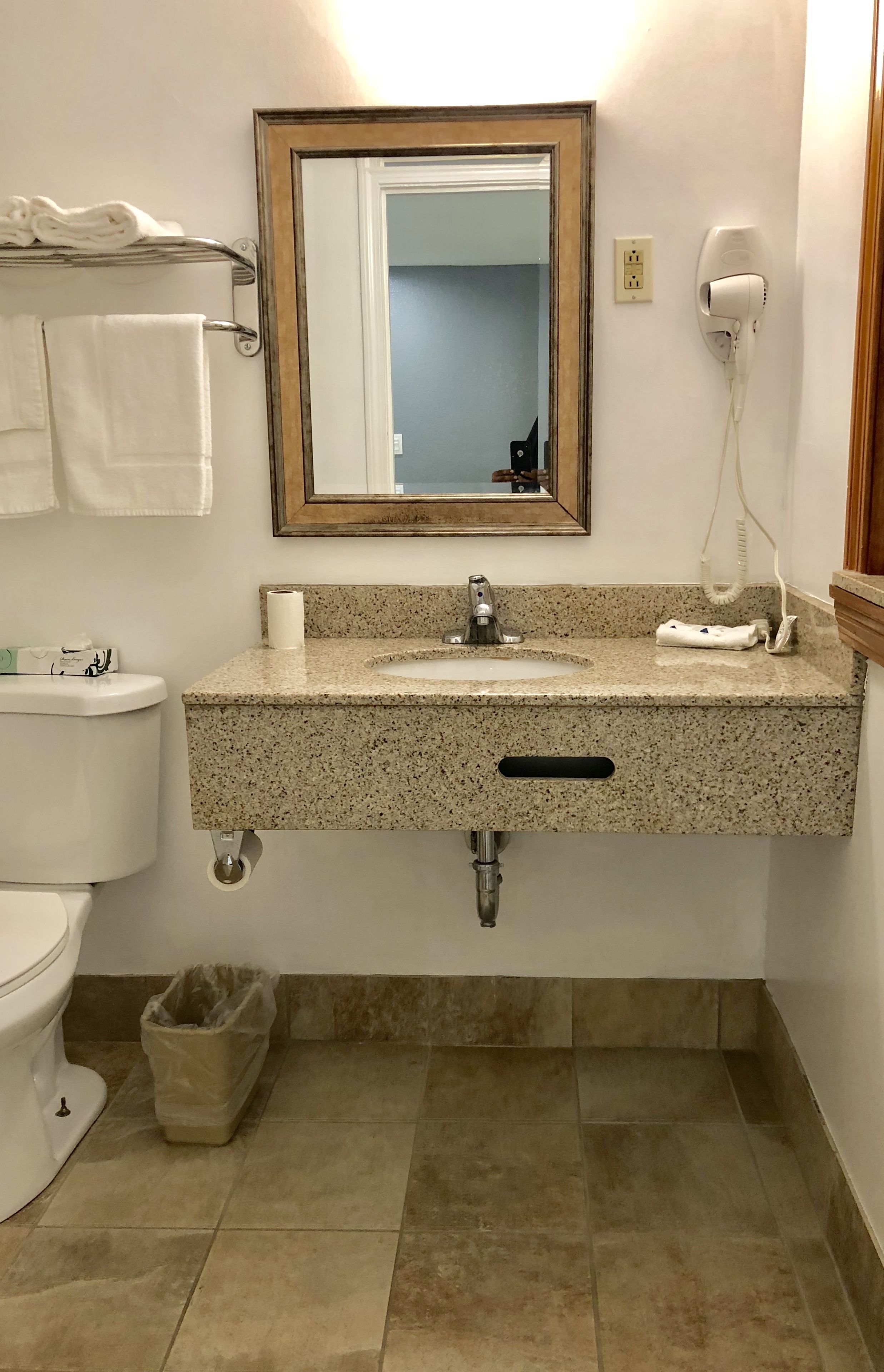 A bathroom with a granite countertop sink, a mirror, a toilet, and a trash bin.