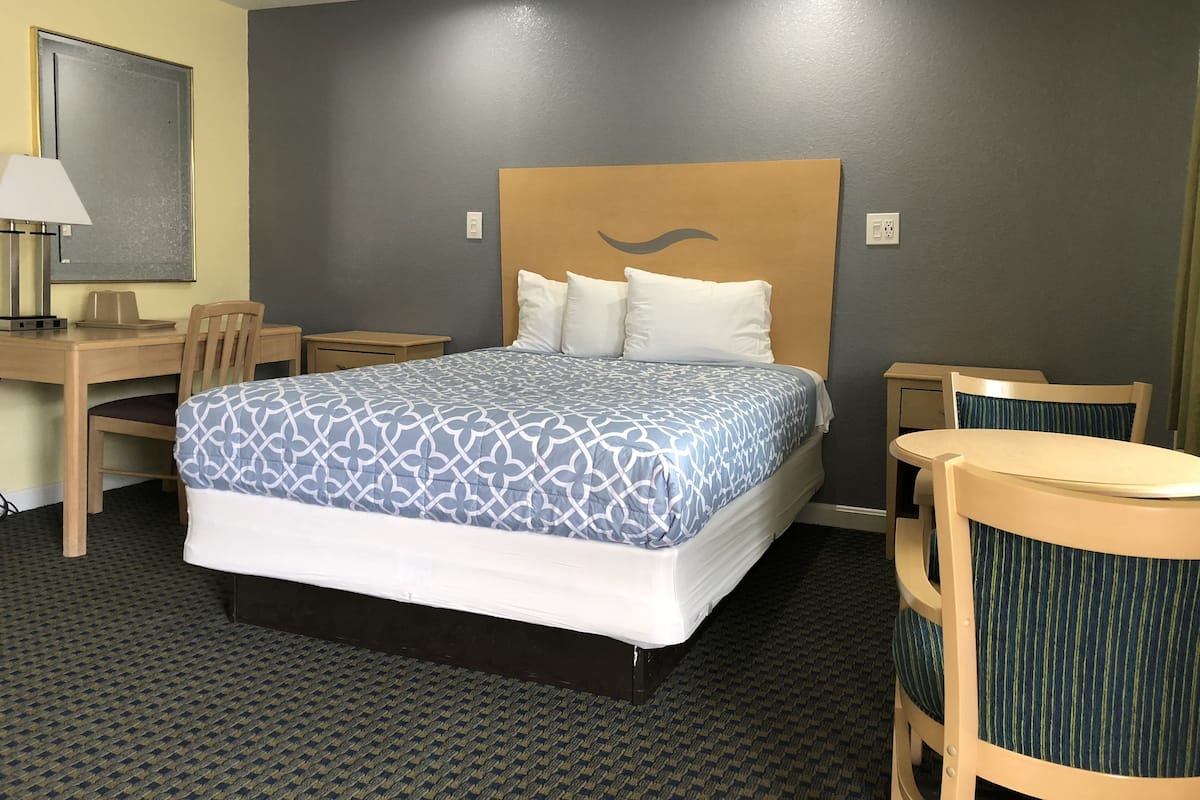 A hotel room with a large bed, a desk, a chair, and a small table.