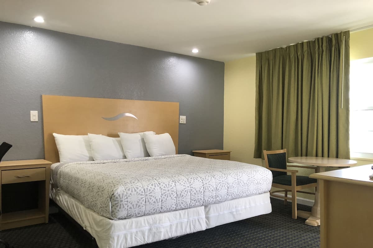 A hotel room with a large bed, a desk, a chair, and a window with curtains.