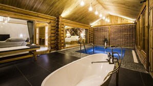 Ein rustikal eingerichtetes Zimmer im Chalet-Stil mit einer großen Badewanne, einer Massageliege und einem kleinen Bett.