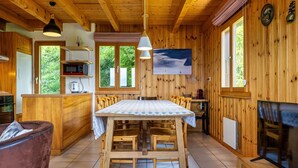 Interior de una cabaña de madera con una mesa de comedor, sillas, una zona de cocina y una chimenea.