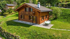 Una cabaña de madera con balcón, rodeada de exuberante vegetación y colinas.