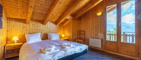 A wooden cabin bedroom with a large bed, two bedside tables with lamps, and a view of the outdoors through a sliding door.
