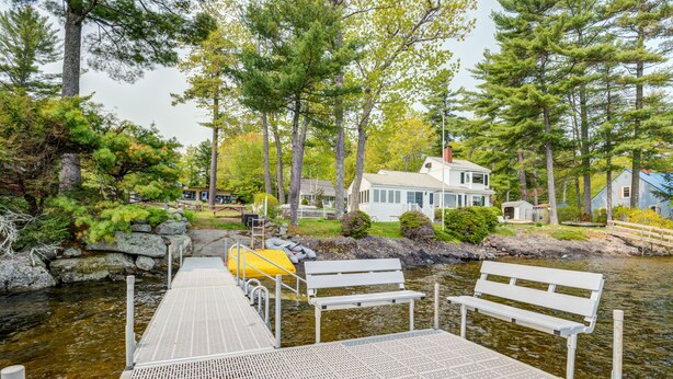 A wooden dock leading to a house by a lake, with benches and a small shed. - LOVELY, LUXURY, NEW BIG SEBAGO HOUSE, WATER ACCESS,
INCLUDES DOCK & MOORING  (Standish)