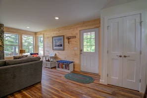 Relax in this inviting living room with a sofa, table, and bookshelf, offering a peaceful view of the surrounding trees.