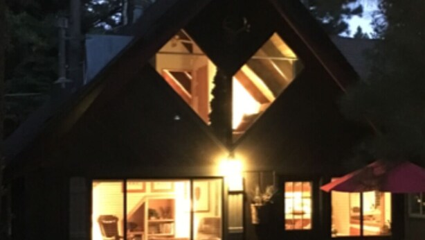 Een blokhut met een groot centraal raam en een kleiner zijraam, beide verlicht.