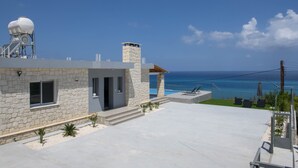 Une maison moderne avec une façade en pierre, une cheminée et un balcon donnant sur l’océan.