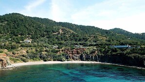 Une région côtière caractérisée par des eaux turquoise et limpides, une plage de sable et un paysage montagneux en arrière-plan.