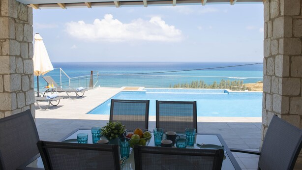 Une vue sur la piscine, avec une vue dégagée sur l’océan, des chaises longues et une table dressée avec des boissons et des fruits.