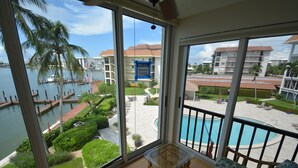 A balcony with a view of a pool, palm trees, and a notice sign.
