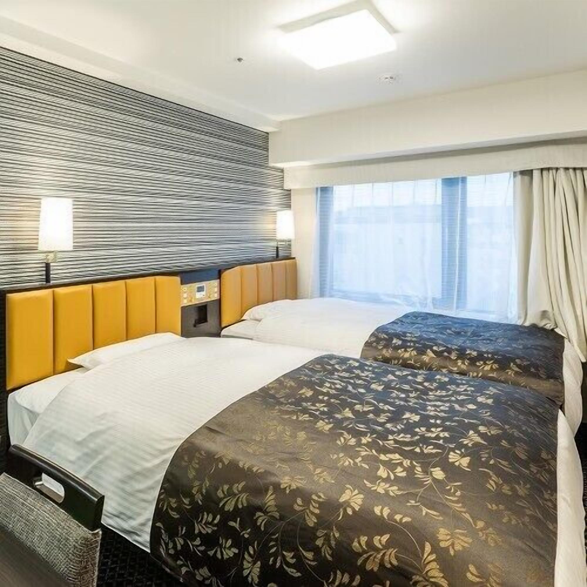 A hotel room with two beds, a headboard, a nightstand, a lamp, and a window with curtains.
