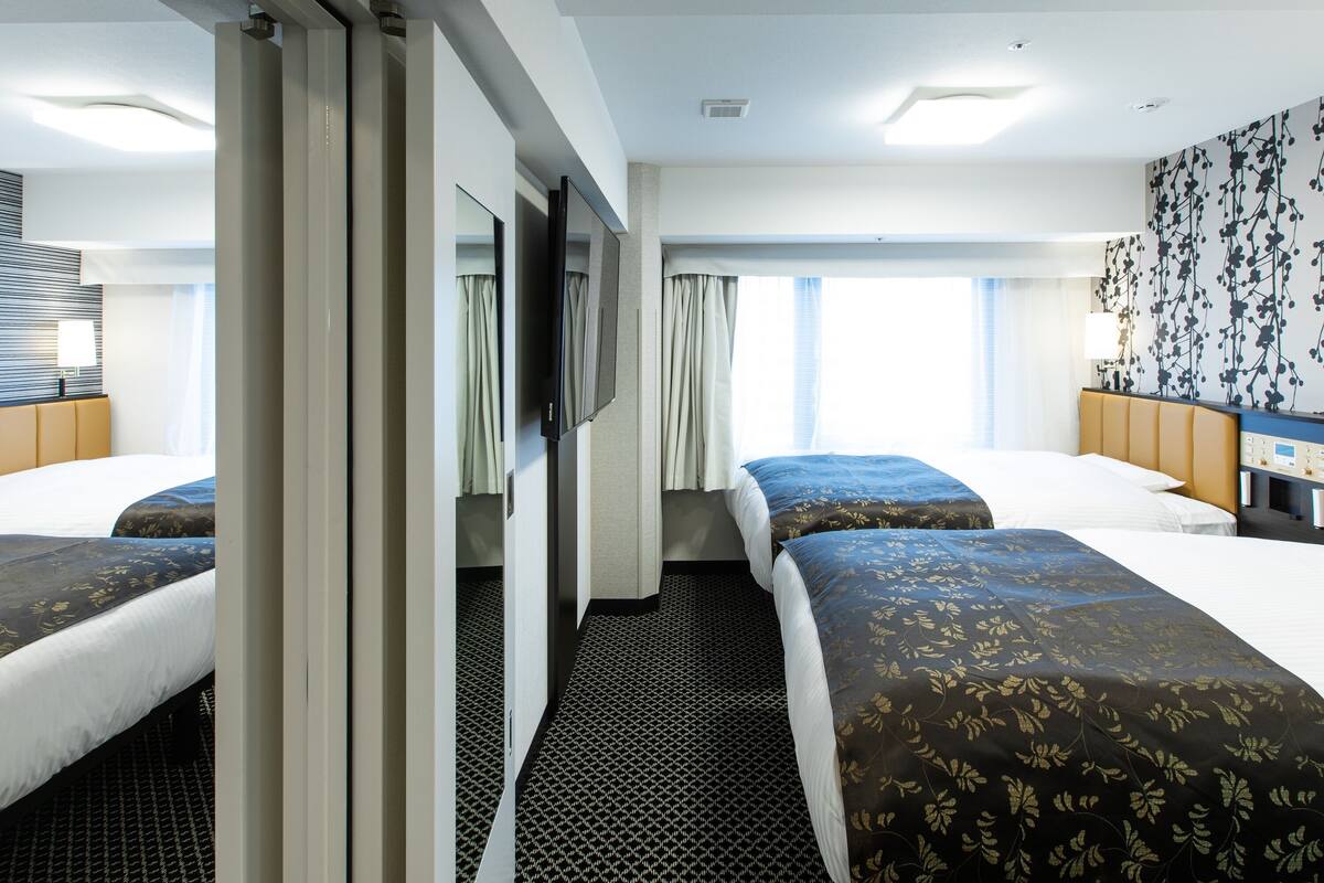Habitación de hotel con dos camas, televisión de pantalla plana, minibar y un amplio ventanal con cortinas.