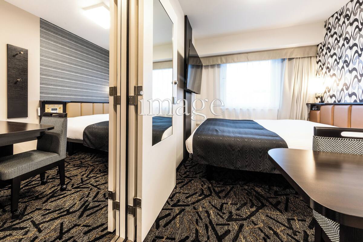 Habitación de hotel con dos camas, un escritorio, una silla, un televisor y un espejo grande.