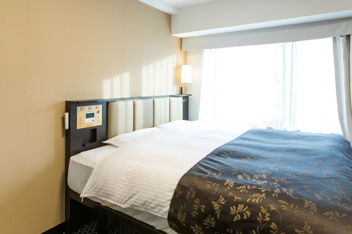 Ein Hotelzimmer mit Bett, Bedienfeld, Fenster mit Vorhängen und einer Wandleuchte.