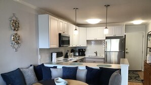 A compact kitchen with white cabinets, a microwave, a stove, and a refrigerator. There is a dining area with a table and chairs, and a bench with cushions. - North Myrtle Beach Vacation Get Away (North Myrtle Beach)