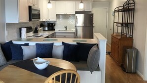 A modern kitchen with white cabinets, a stainless steel refrigerator, and a dining area with a wooden table and a bench. - North Myrtle Beach Vacation Get Away (North Myrtle Beach)