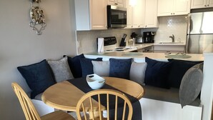 A modern kitchen with white cabinets, a microwave, a coffee maker, and a refrigerator. There is a round wooden table with two chairs. - North Myrtle Beach Vacation Get Away (North Myrtle Beach)