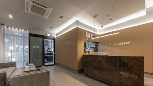 A hotel reception area with a marble reception desk, a sofa, and a television screen. - Brown Dot Hotel Deokcheon (Busan)