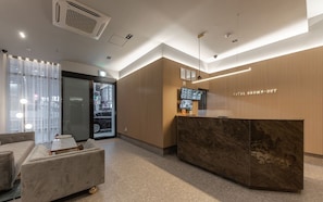 A hotel reception area with a marble reception desk, a sofa, and a television screen. - Brown Dot Hotel Deokcheon (Busan)