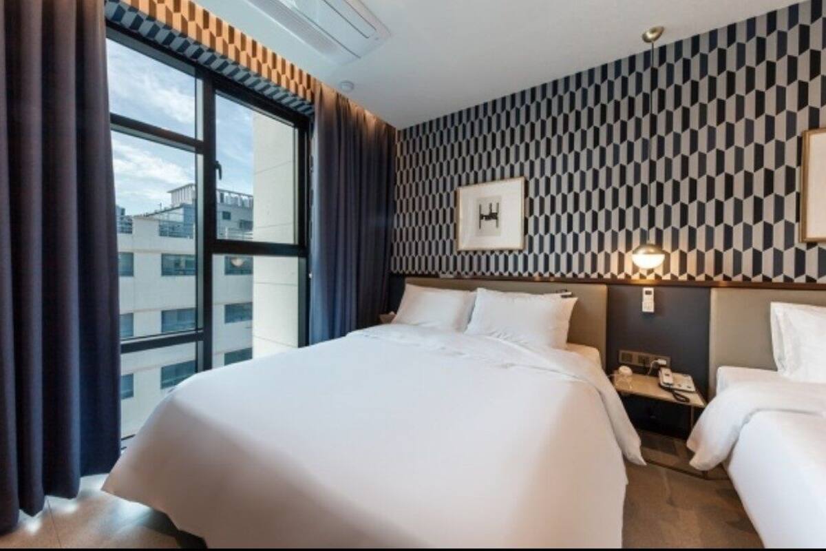 A hotel room with a large bed, two bedside tables, a window with curtains, a patterned wall, and a framed picture.